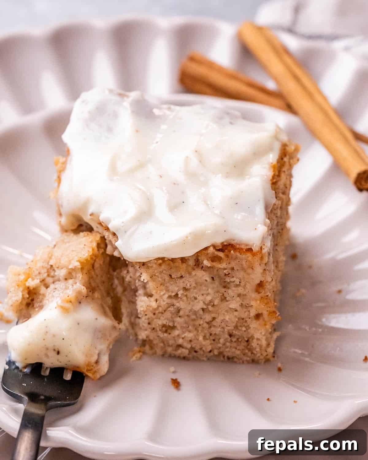 Cinnamon Swirl Dream Cake 8 A single, perfectly cut slice of Cinnamon Roll Cake elegantly presented on a white fluted plate, highlighting its moist texture and generous glaze.