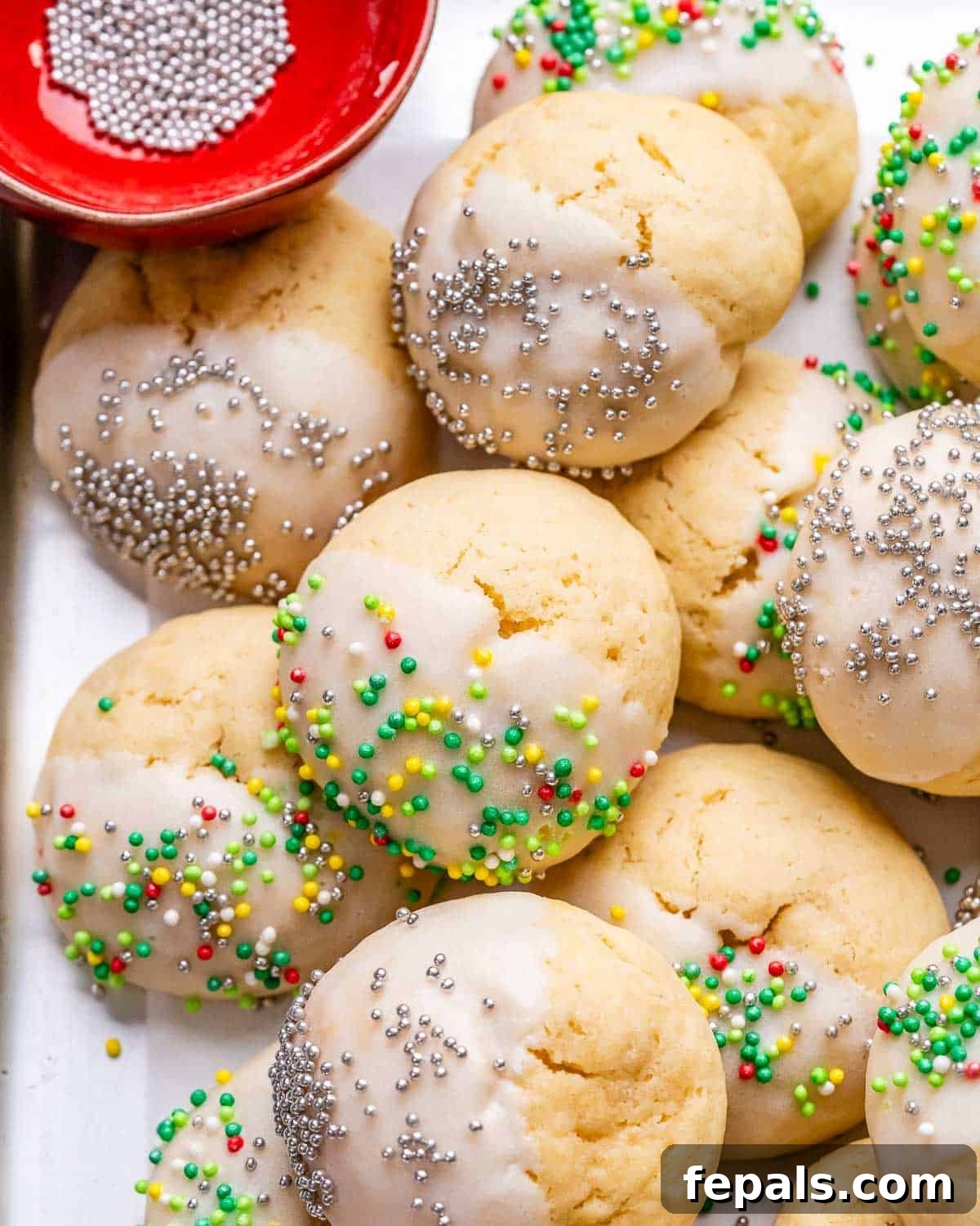 Sweet Italian Christmas Delights 8 Baked Italian Christmas Cookies with white glaze and rainbow sprinkles on a parchment-lined sheet pan.
