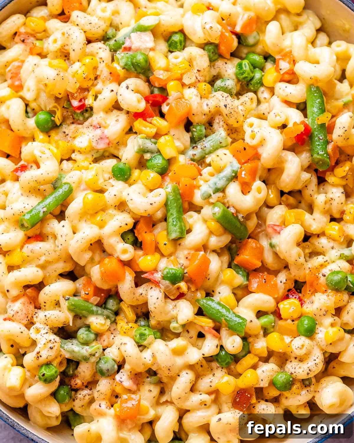 Vibrant Veggie Mac 7 A close-up, appetizing image of homemade veggie mac and cheese in a white bowl, highlighting the creamy texture and colorful bits of carrots, peas, and green beans.