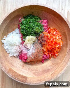 a bowl with ground beef, chopped parsley, diced onion, diced pepper, and seasonings.