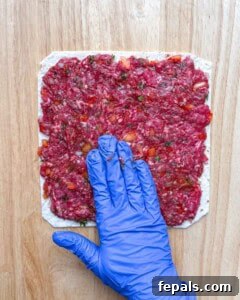 ground beef being spread over the tortilla.