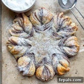 A baked cinnamon roll snowflake on a sheet pan, beautifully topped with powdered sugar.