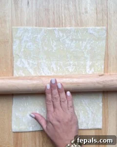 A hand rolling out a puff pastry sheet using a rolling pin on a floured surface.