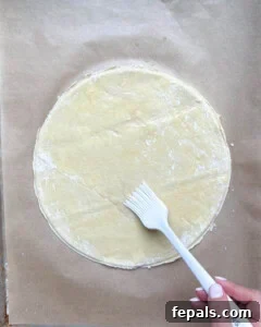 Melted butter being brushed onto a single sheet of puff pastry.