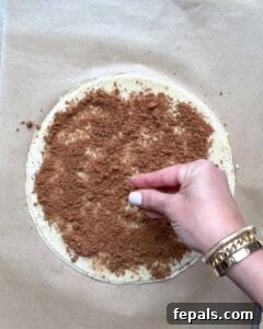 Cinnamon sugar being sprinkled evenly over the buttered puff pastry layer.