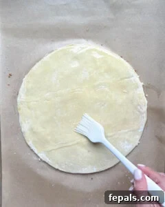 Melted butter being brushed over the second layer of puff pastry, preparing for more cinnamon sugar.