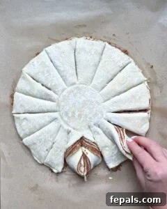 Hands demonstrating the twisting of two adjacent puff pastry strands to form part of the snowflake design.