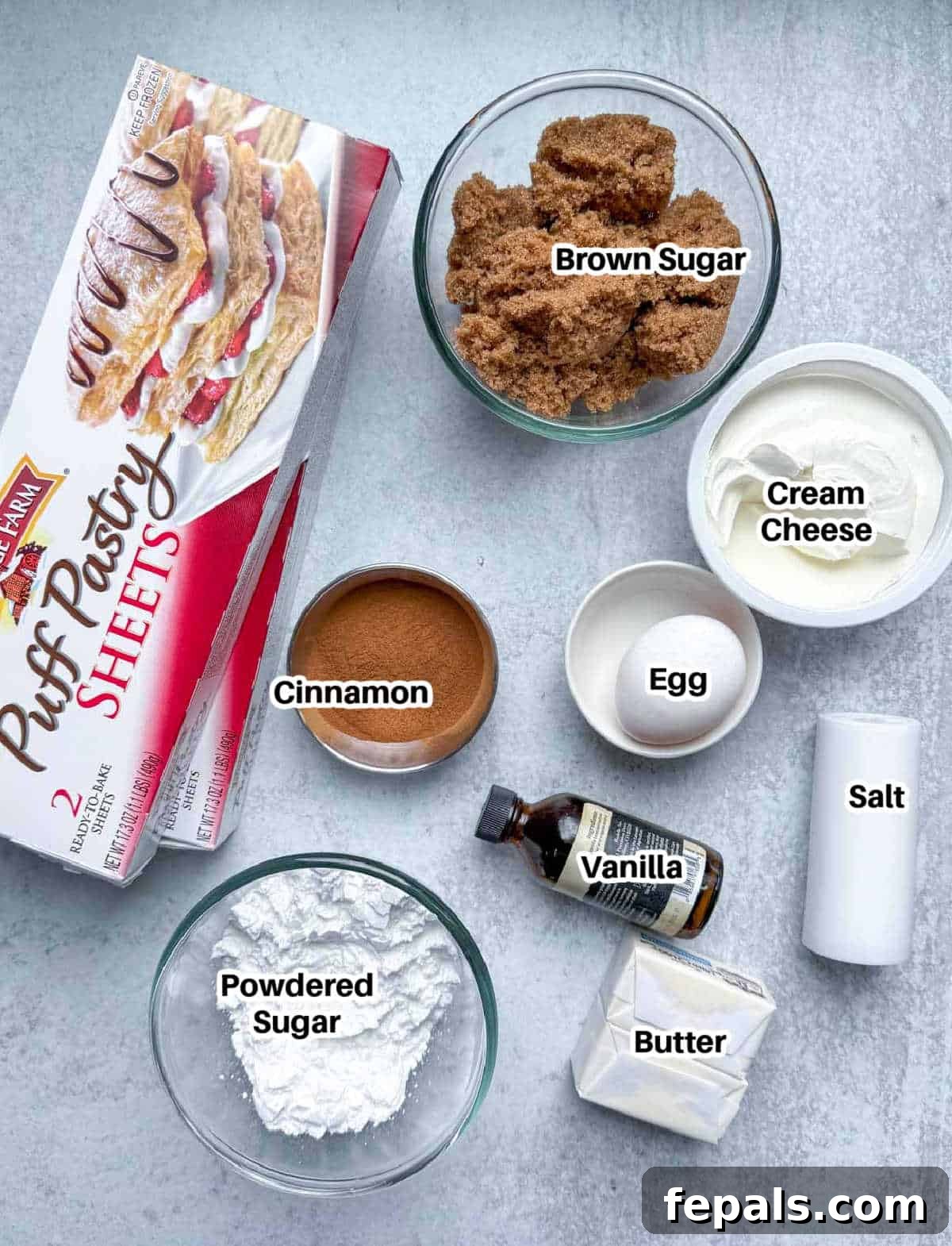 A selection of ingredients laid out, including puff pastry, cinnamon, brown sugar, butter, and an egg, ready for baking.