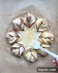 Egg wash being carefully brushed over the snowflake-shaped puff pastry before baking.