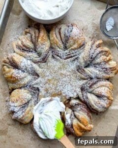 Cream cheese frosting being artfully applied over the baked puff pastry snowflake.