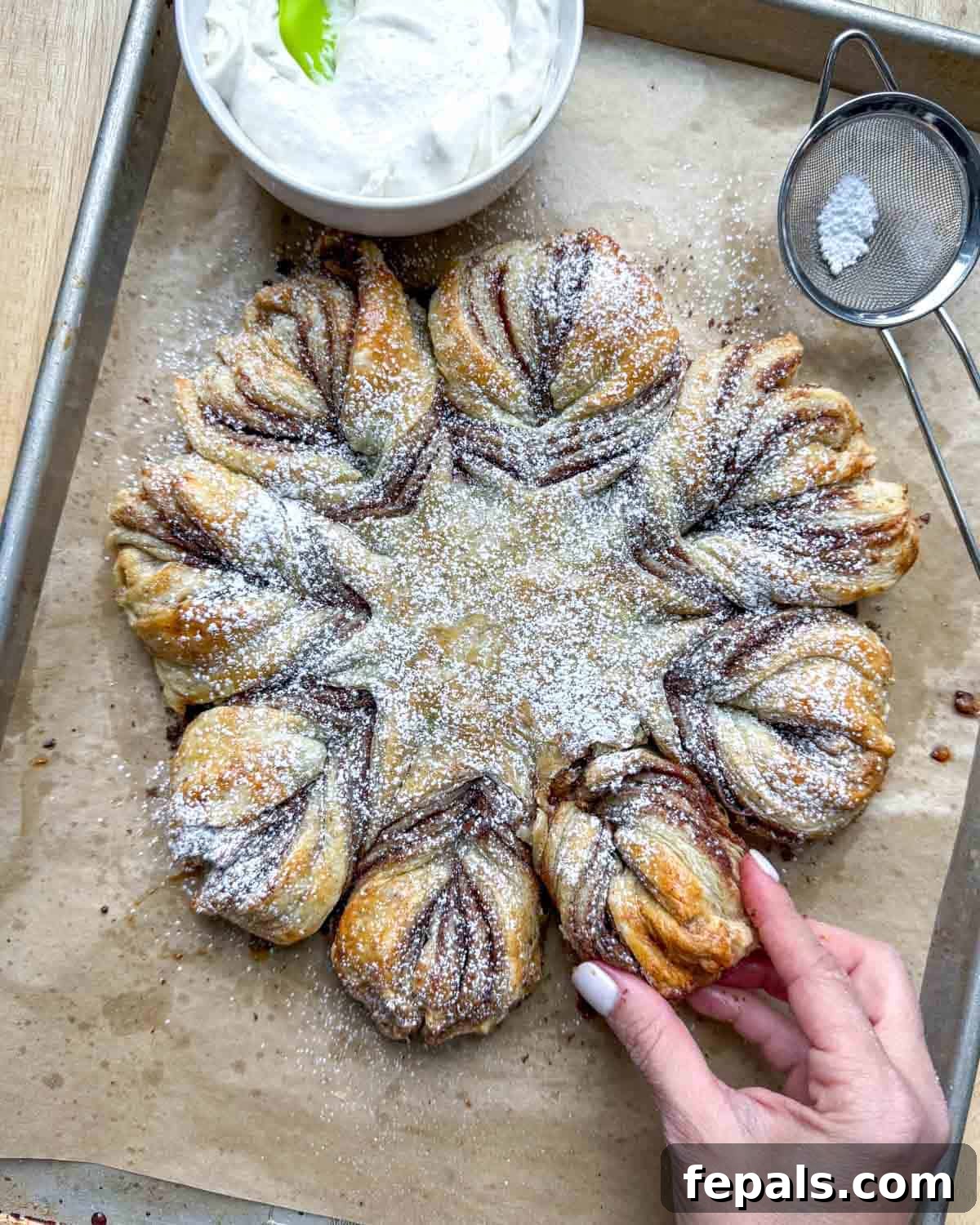 A hand reaching to pull a piece from the freshly baked and frosted cinnamon roll puff pastry snowflake, showcasing its tempting layers.