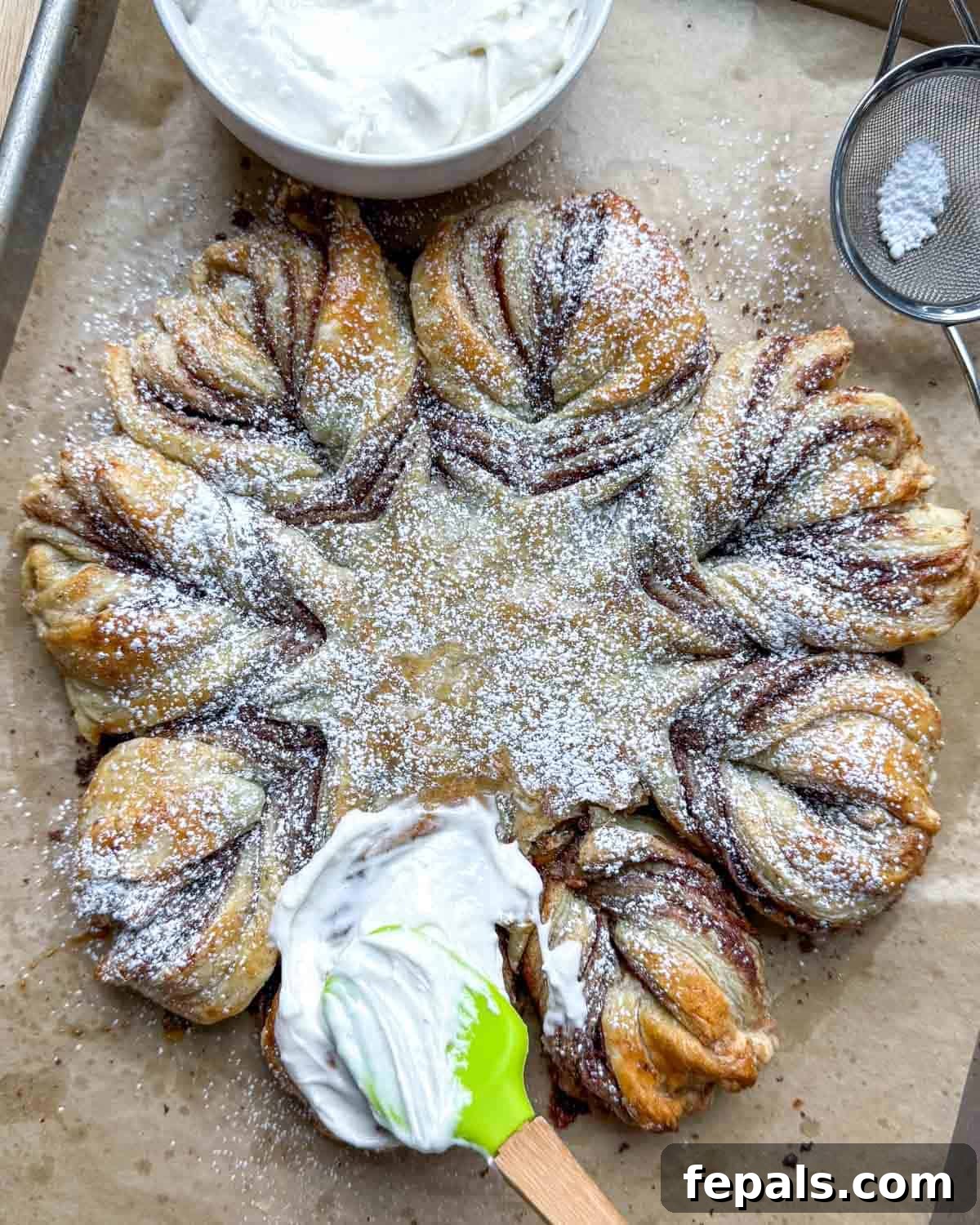 Cream cheese frosting being artfully drizzled over the baked and cooled cinnamon roll puff pastry snowflake.