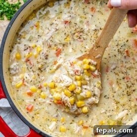 A spoon resting invitingly in a rich chicken corn chowder soup pot, showcasing its creamy texture and hearty ingredients.