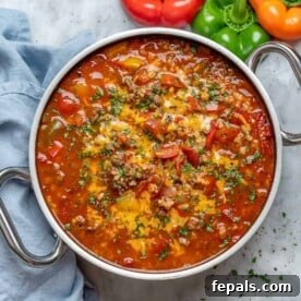A round, large pan filled with vibrant stuffed pepper soup, garnished generously with shredded cheese and fresh chopped parsley.