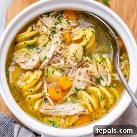 A close-up, inviting top view of classic chicken noodle soup in a white bowl, showcasing its golden broth, perfectly cooked egg noodles, and tender chunks of chicken.