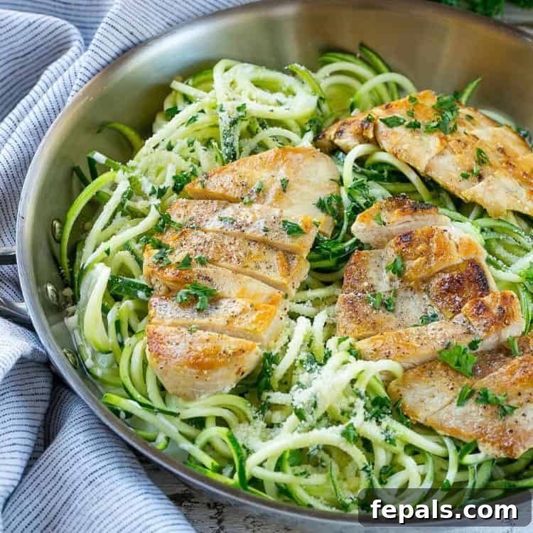 Healthy Light and Creamy Chicken Alfredo Recipe Healthy chicken alfredo zoodles in pan with succulent chicken breasts, garnished with fresh herbs, ready to serve.