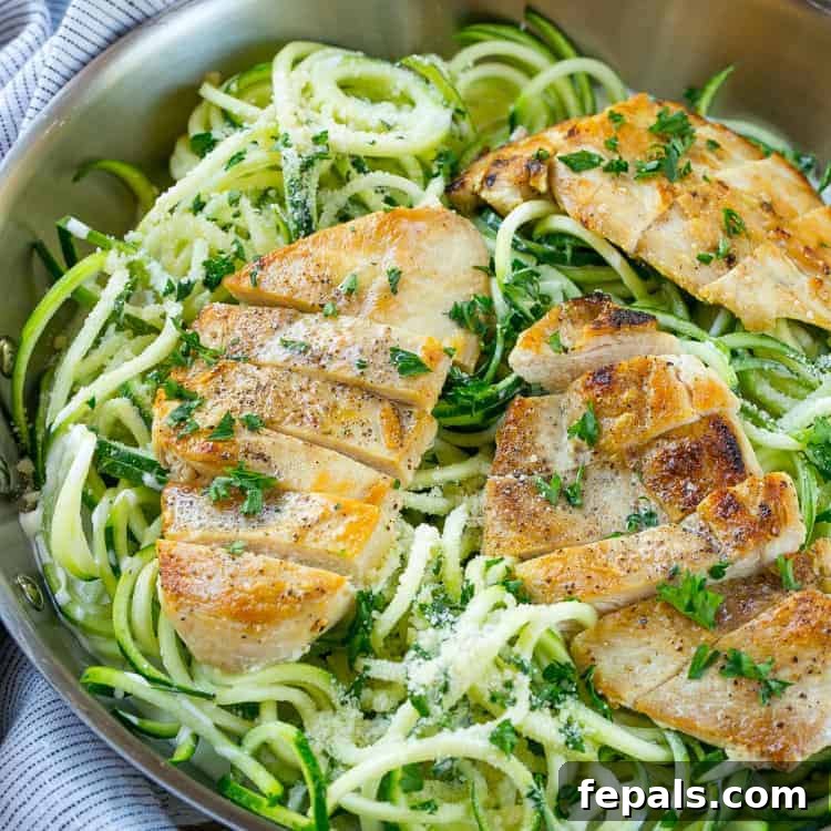 Low-Carb Chicken Alfredo Recipe Close-up of healthy chicken alfredo zoodles in a pan, topped with freshly chopped parsley and sliced chicken.