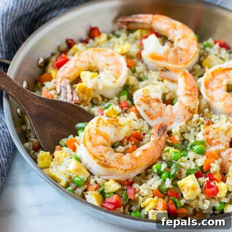 Healthy Low Carb Shrimp Cauliflower Fried Rice Recipe: A Quick & Delicious Meal Shrimp Cauliflower Fried Rice with vibrant vegetables cooked in a silver pan, stirred with a wooden spoon.