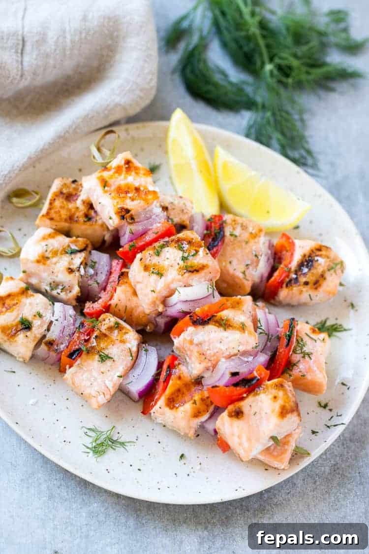 Salmon Skewers on a white plate with lemon and veggies, showcasing perfectly grilled fish and colorful vegetables