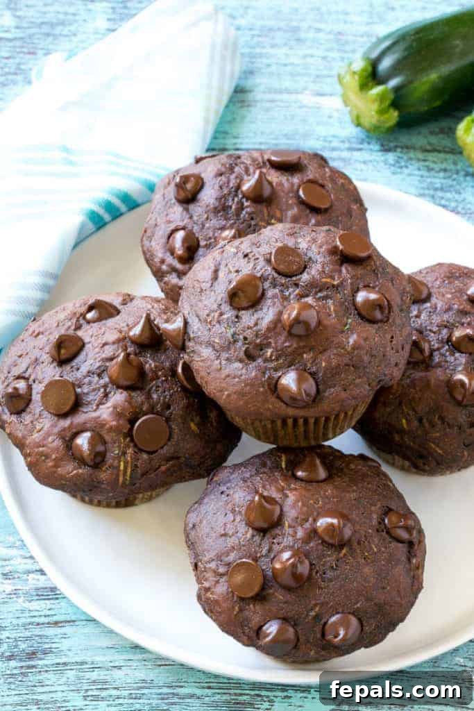 Stacked healthy chocolate zucchini muffins on a white plate, showcasing their rich color and fluffy texture.