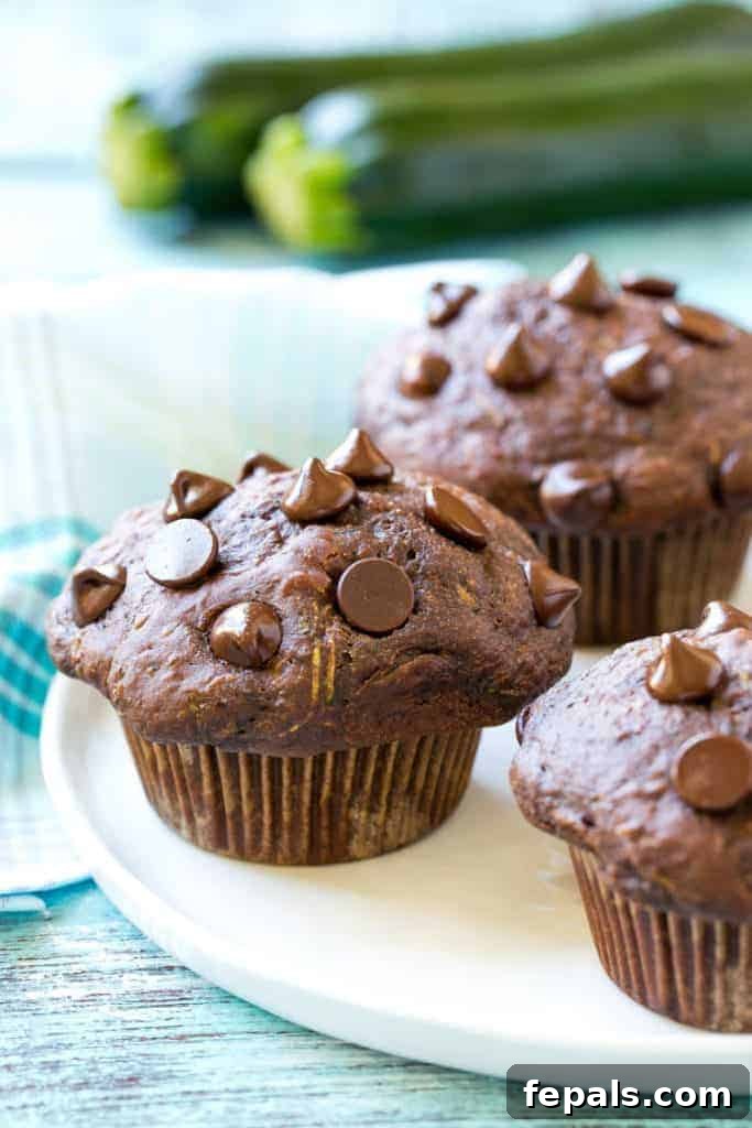 Close-up side view of a stack of moist chocolate zucchini muffins on a white plate, highlighting their rich color and delicious appeal.