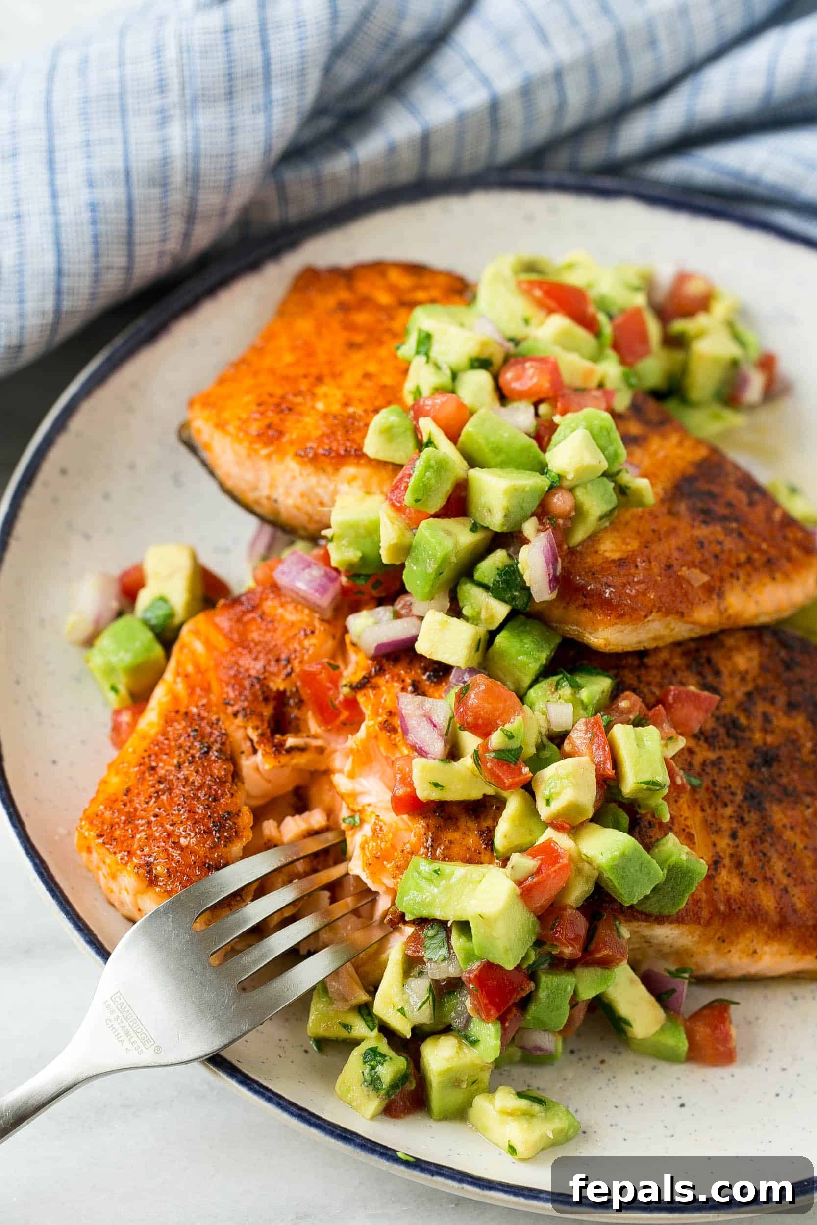 Beautifully cooked pan-seared salmon, served with a generous portion of avocado salsa and a fork on a white plate, ready to be savored.