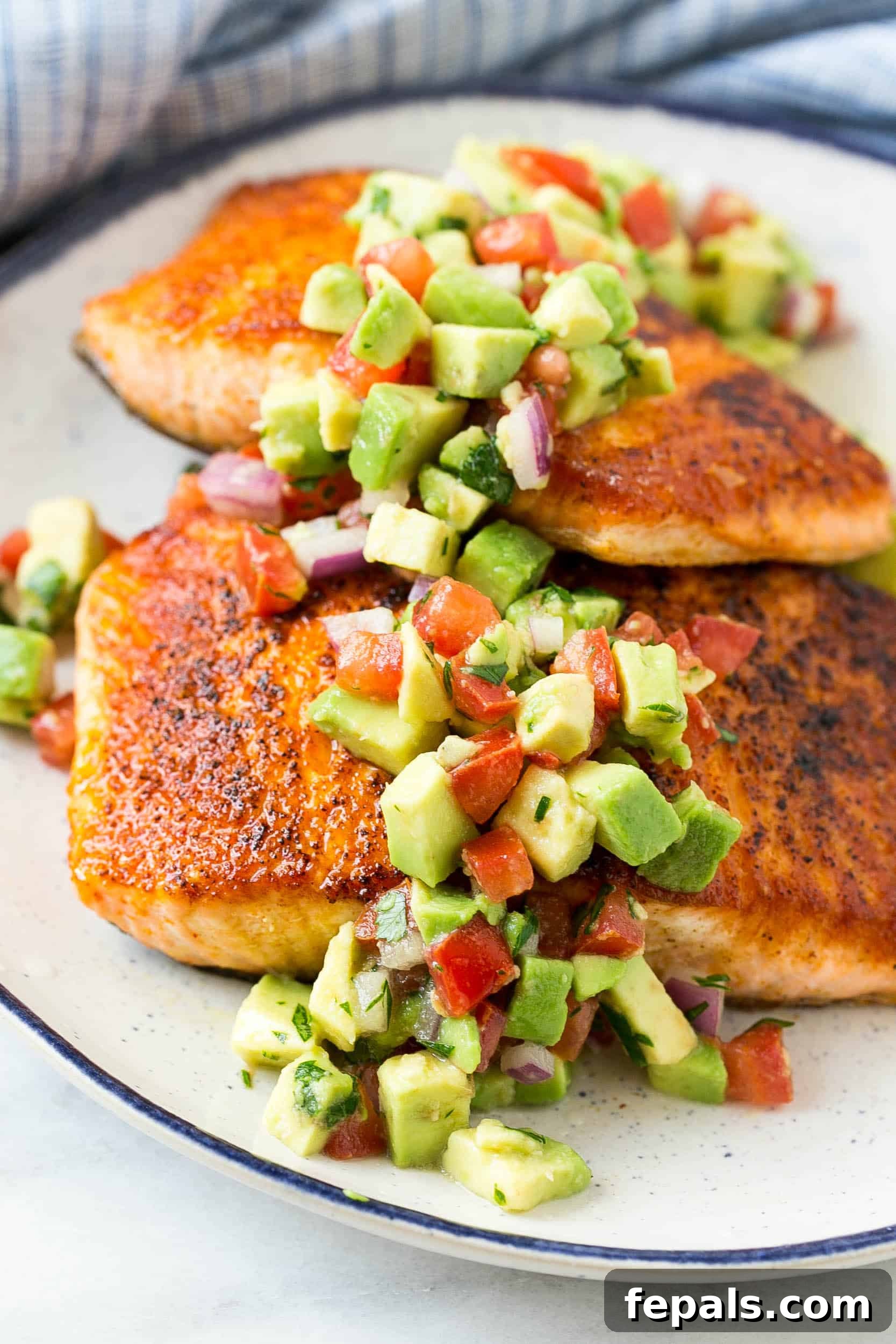 A stunning presentation of salmon with avocado salsa, elegantly arranged on a white plate.