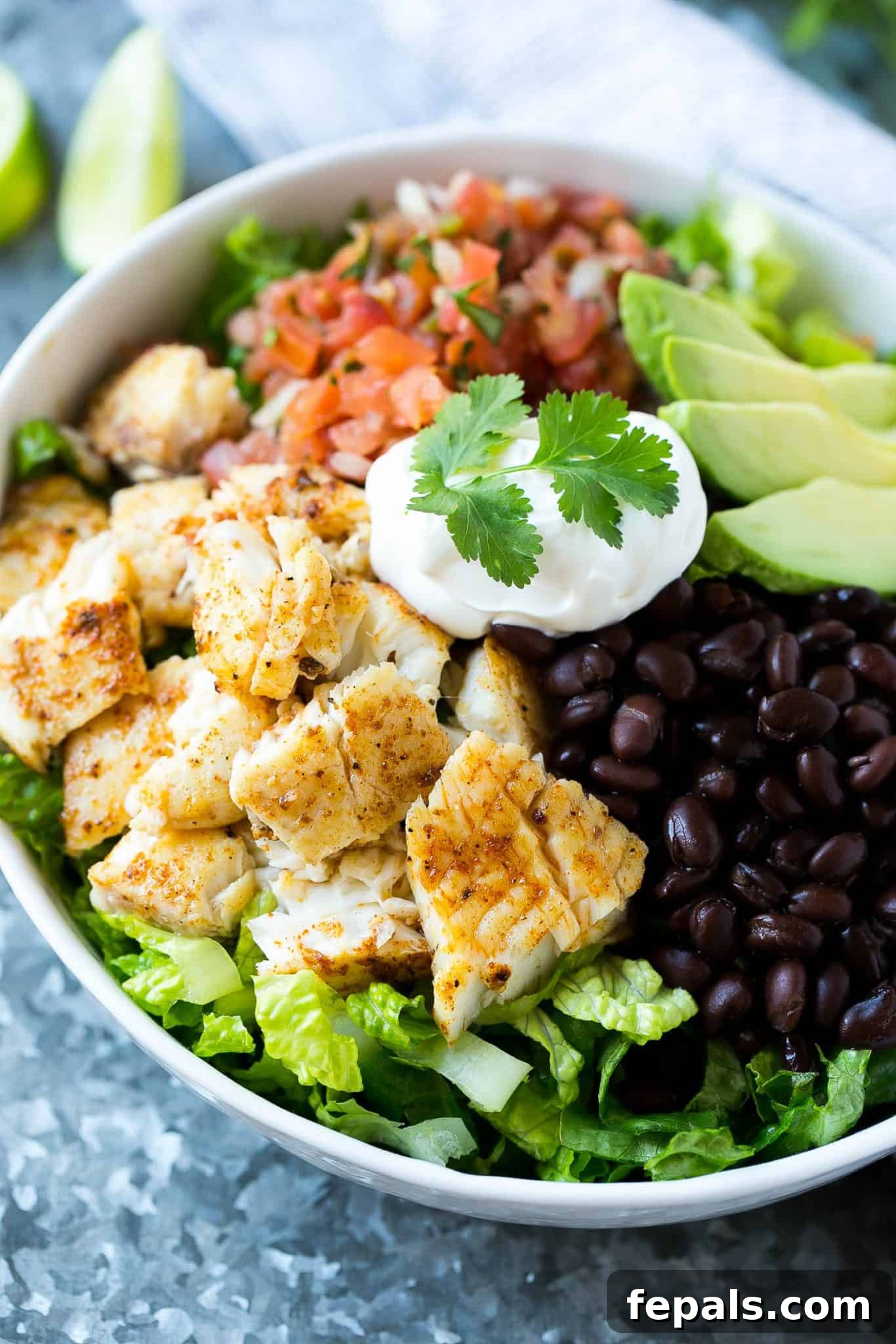 Easy Fish Taco Salad Bowl A close-up of the fish taco salad bowl, showcasing the creamy sour cream drizzle, vibrant cilantro, and perfectly cooked fish amidst a colorful mix of black beans, salsa, and avocado.