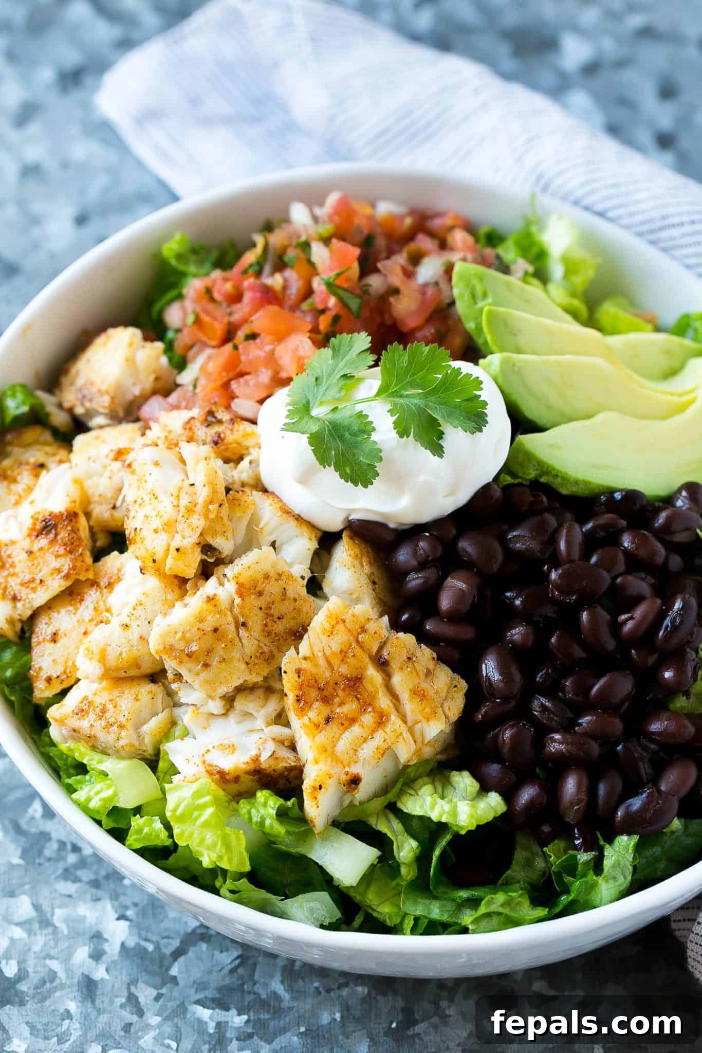 Healthy Fish Taco Salad Bowl Recipe A simple yet elegant taco salad in a white bowl, topped with a swirl of sour cream and fresh cilantro, highlighting the minimal beauty of the dish.