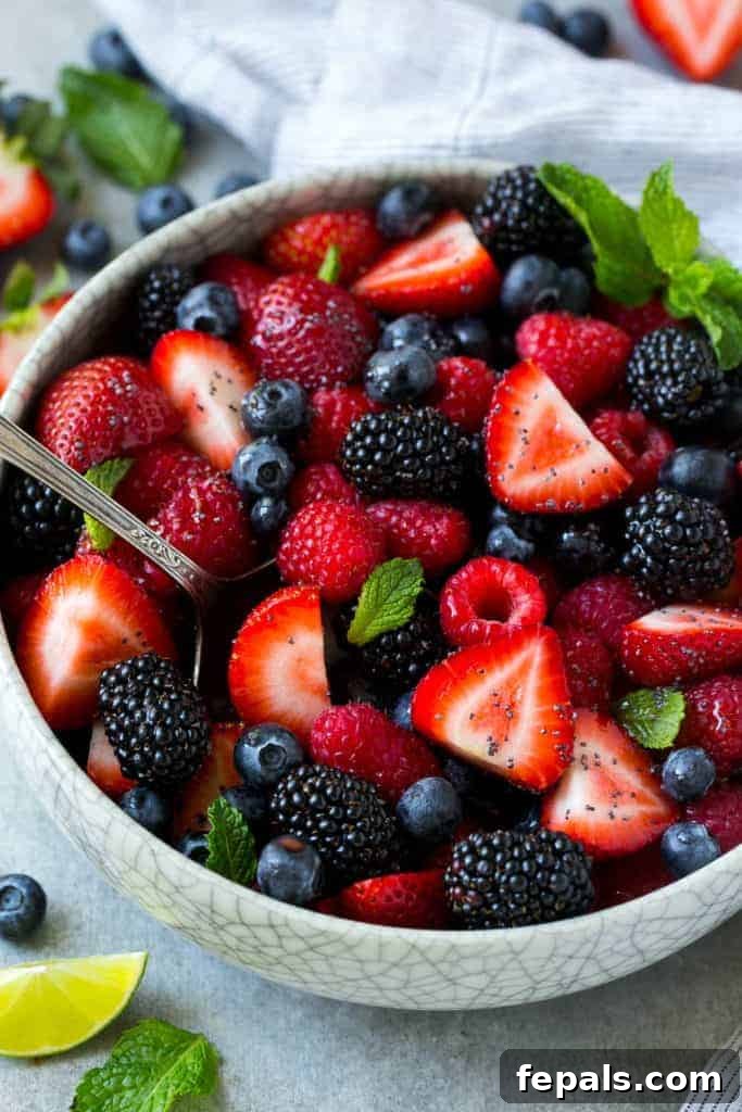 top view of berry fruit salad in a round white bowl with mint and lime wedge garnish