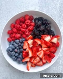 Chopped strawberries, blueberries, raspberries, and blackberries placed in a white bowl.