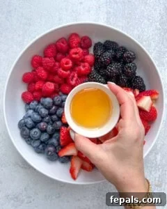 honey being added over chopped berries in a bowl.