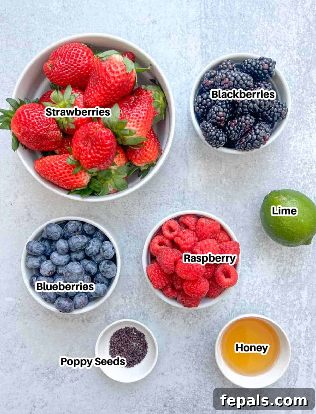 ingredients to make a berry salad, including fresh strawberries, blueberries, blackberries, lime, honey, and poppy seeds.