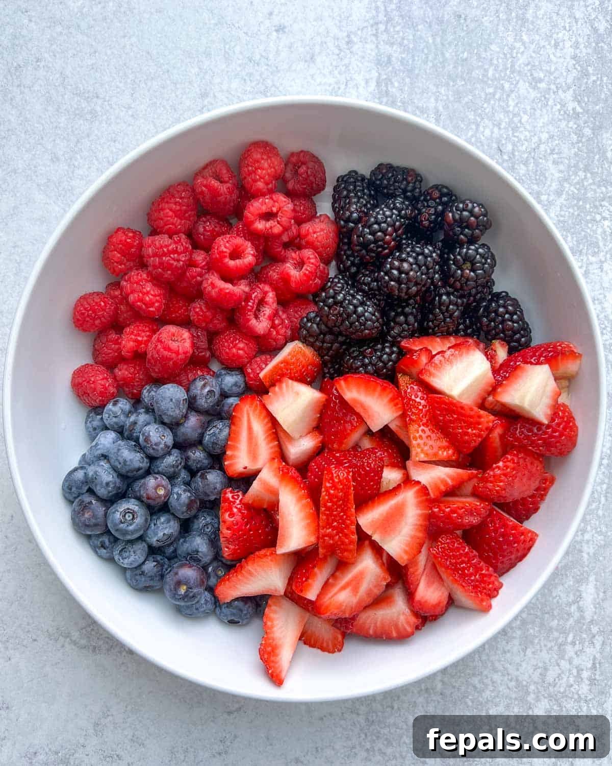 Chopped strawberries, blueberries, raspberries, and blackberries placed in a white bowl, ready to be dressed.