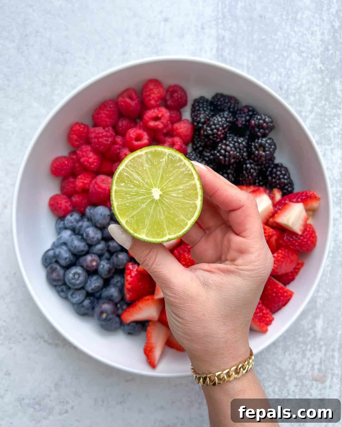 hand holding half a lime over a bowl of berries, squeezing juice.