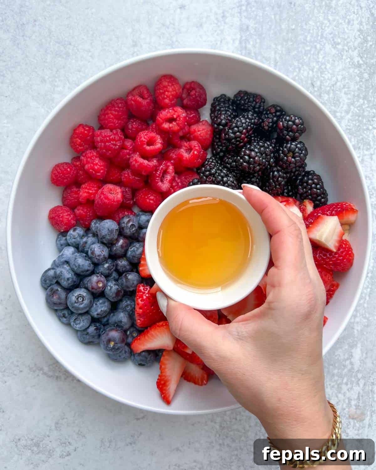 honey being added over chopped berries in a bowl, creating a glossy sheen.