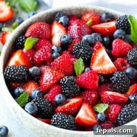 side shot of a white bowl with berries fruit salad topped with fresh mint leaves