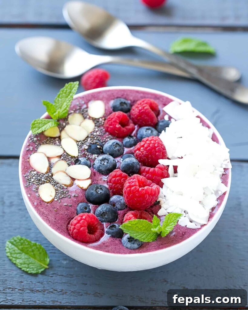 Berry Burst Bowl 4 A tempting berry smoothie in a elegant white round bowl, artfully adorned with an array of fresh fruits and crunchy coconut flakes, ready to be enjoyed.