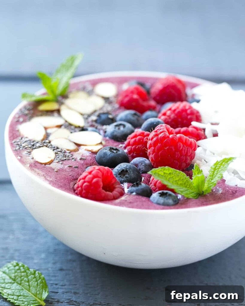 Berry Burst Bowl 6 An appetizing side shot of a rich berry smoothie bowl, elegantly topped with an assortment of fresh berries and crisp sliced almonds, highlighting its wholesome appeal.