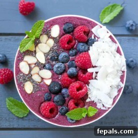 Berry Burst Bowl 8 top view of a white round bowl with berry coconut smoothie topped with fresh berries, sliced almonds, and shaved coconut