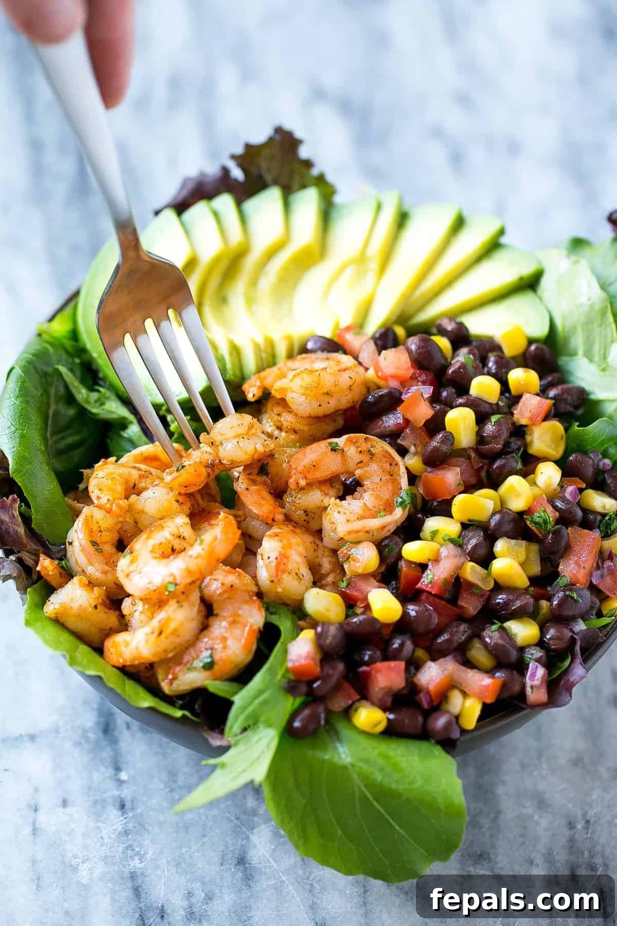 Fork reaching into a vibrant Mexican shrimp salad bowl with seasoned shrimp, black bean salsa, and creamy avocado slices.