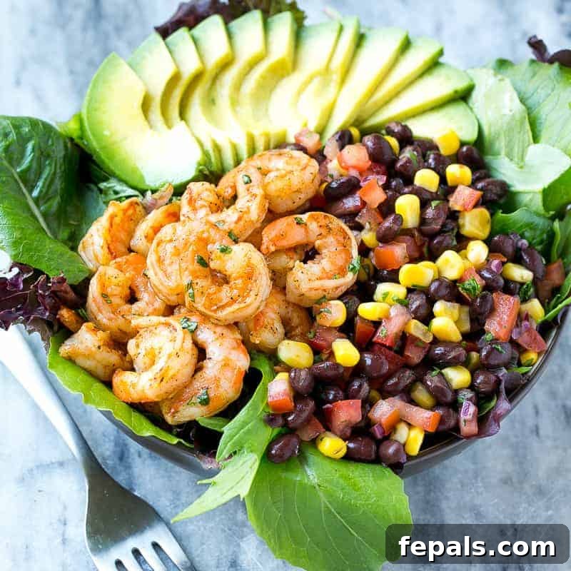 Close-up of a colorful salad bowl featuring perfectly cooked shrimp, a medley of black bean and corn salsa, and fresh avocado.