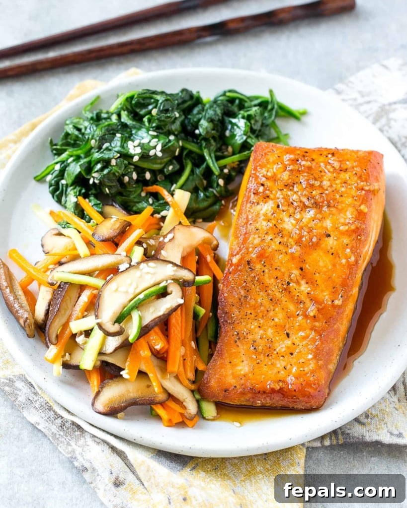 Side view of a perfectly seared salmon fillet on a white plate, accompanied by vibrant sautéed vegetables and spinach, showcasing the moist interior.