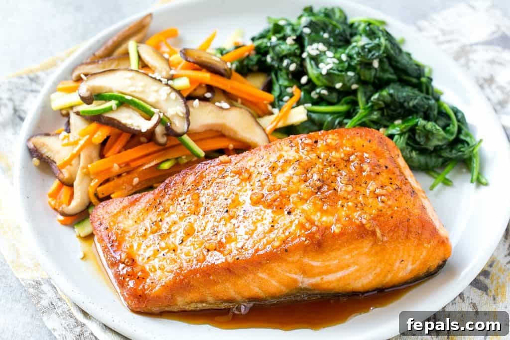 Side view of a perfectly pan-seared honey garlic salmon fillet generously coated in the sweet and savory sauce, served on a plate with sautéed vegetables.