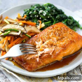 Fork flaking a seared salmon on a white plate with a side of sautéed veggies and spinach, illustrating the perfect doneness of the fish.