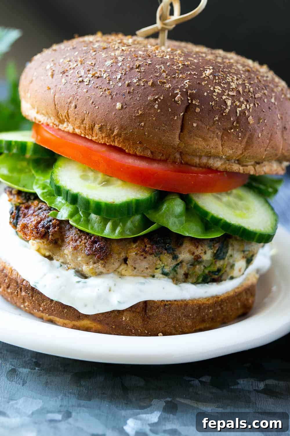 Gourmet turkey burger with spinach and feta cheese, garnished with fresh lettuce, tomato, and a side of creamy tzatziki sauce, served on a plate.