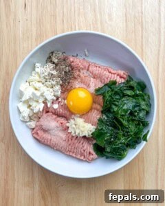 Ground turkey, egg, spinach, feta cheese, and seasonings, added to a bowl.