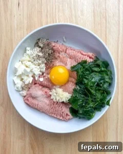 Ground turkey, egg, spinach, feta cheese, and seasonings, added to a bowl.