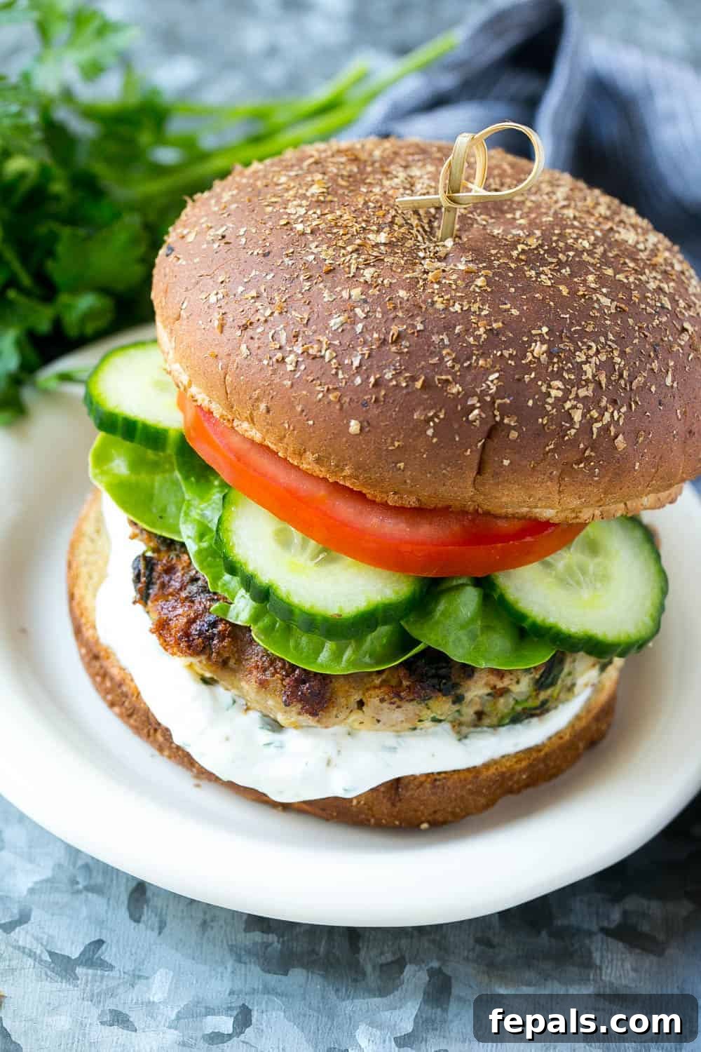 A delicious turkey burger with spinach and feta, served on a bun with fresh vegetables and a dollop of tzatziki sauce on the side.