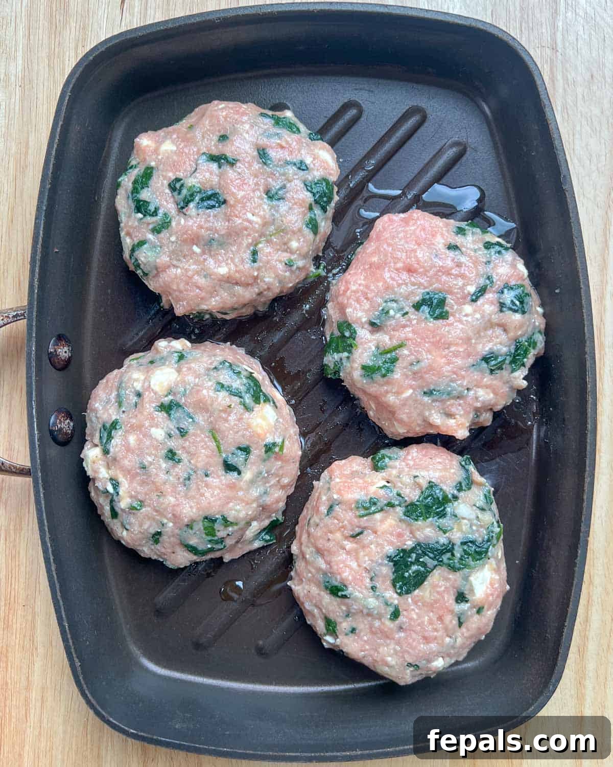 Four perfectly formed turkey burger patties placed in a hot pan with olive oil, ready for cooking on the stovetop.
